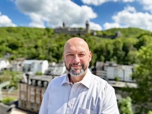 Nahaufnahme des Stadtsprechers Hanno Grundmann, im Hintergrund die Burg Altena, im Sonnenschein bei blauem Himmel.