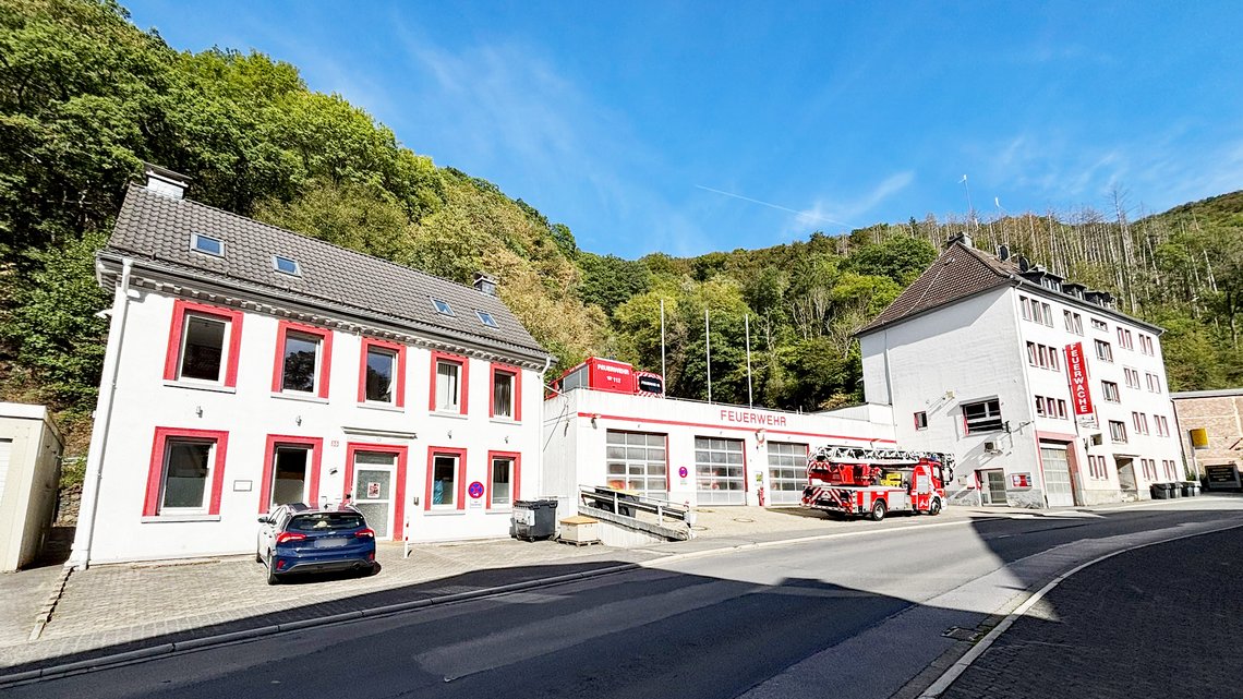 Bild der Feuerwache Altena im Weitwinkelformat bei Sonnenschein vor grünem Wald.