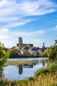 Ein Bild der Ville de Péronne, Partnerstadt von Altena, während einer Mongolfiade, blauer Himmel und Heißluftballons in der Ferne, im Vordergrund Marschland des Somme-Zuflusses "La Cologne".
