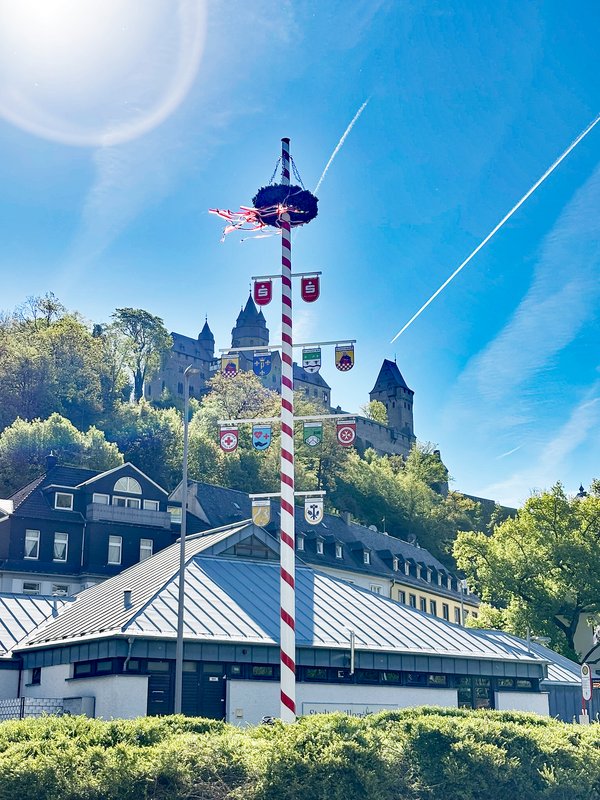 Der im Jahr 2026 neu errichtete Maibaum auf dem Kreisverkehr am Markaner strahlt in der Sonne mit der Burg im Hintergrund.