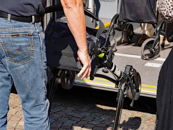 Ein Mann zeigt in einer Nahaufnahme, wie man einen Rollator richtig in den hinteren Einstieg eines Nahverkehrs-Busses reinschiebt.
