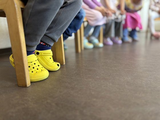 Füße in Reihe von sitzenden Kindern in einer Kindertagesstätte, bunte Schühchen werden getragen.