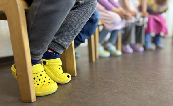 Füße in Reihe von sitzenden Kindern in einer Kindertagesstätte, bunte Schühchen werden getragen.