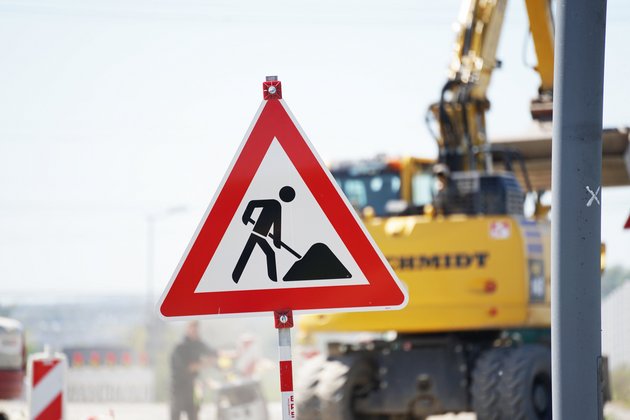 Ein Baustellenschild vor eine Baustelle mit Bagger unscharf im Hintergrund.